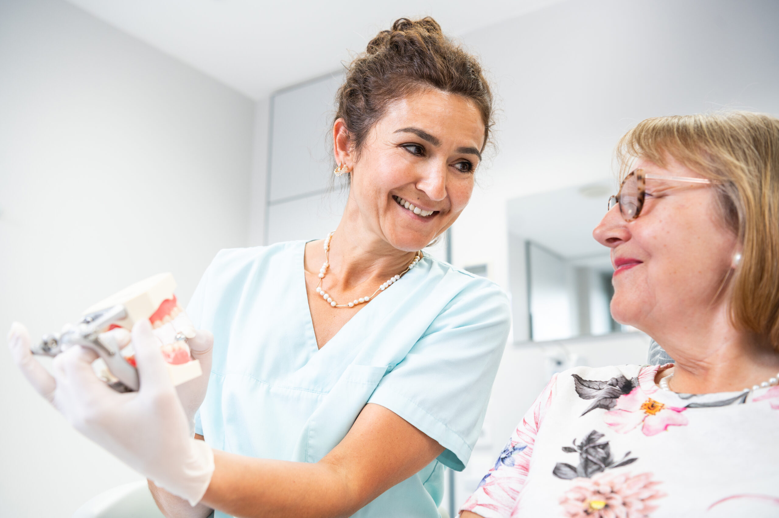 Die Arzthelferin zeigt einer Patientin anhand eines Gebiss Models wie eine Zahnreinigung funktioniert