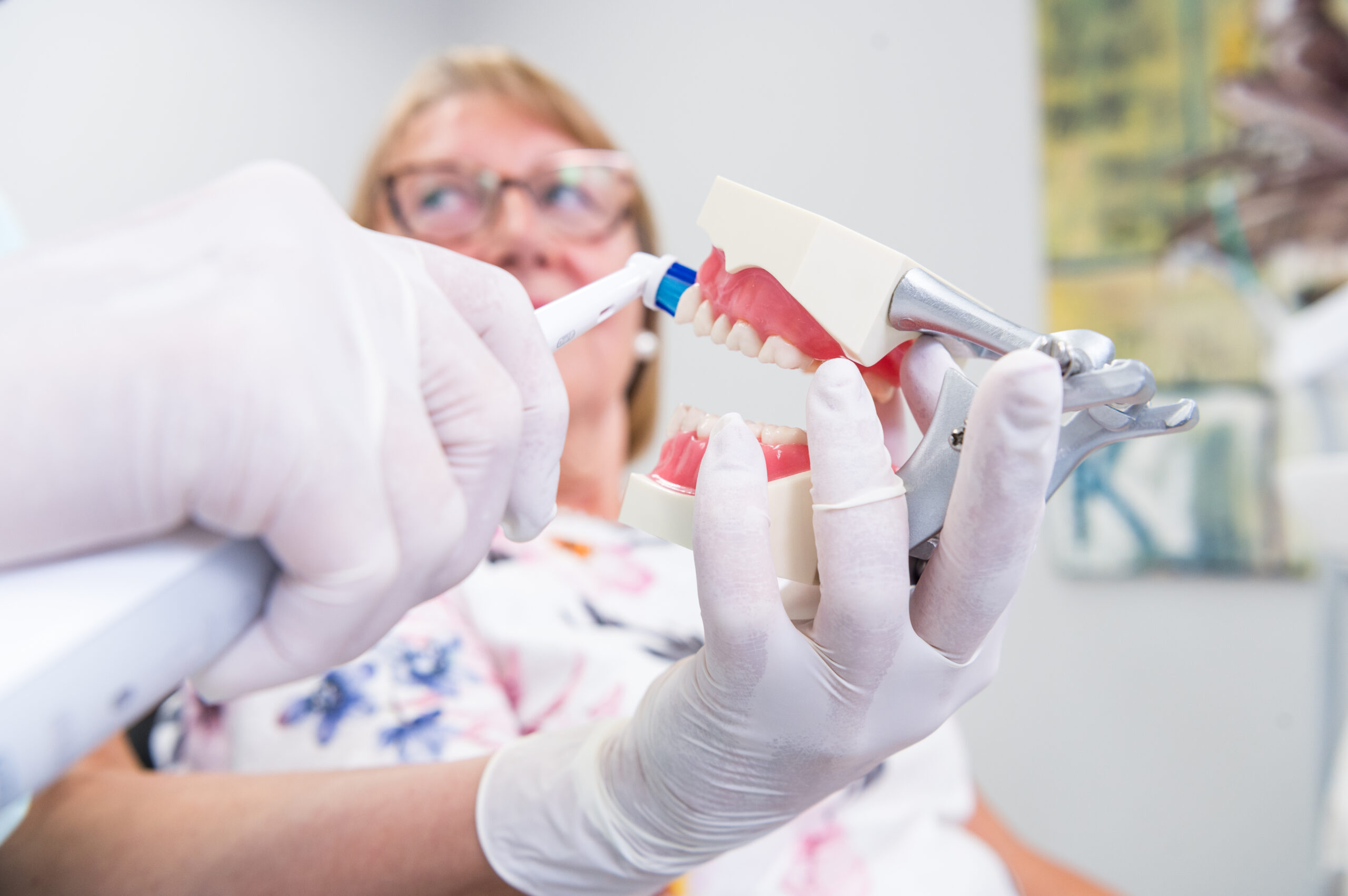 Der Arzt zeigt einer Patientin anhand eines Gebiss Models wie eine Zahnreinigung funktioniert